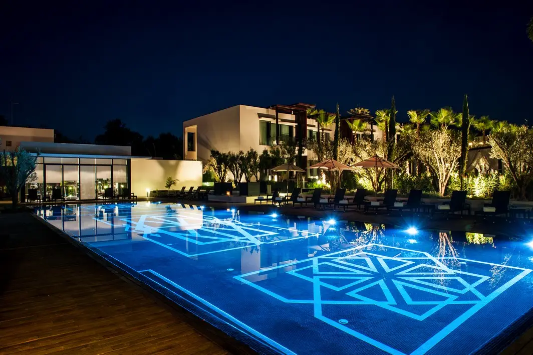 Illuminated outdoor swimming pool with geometric Moroccan design at night, surrounded by palm trees and luxury hotel buildings at STORY Rabat in Morocco.
